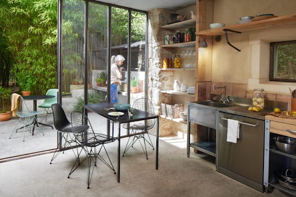 Small kitchen with three black Eames chairs, woman gardening in the back yard
