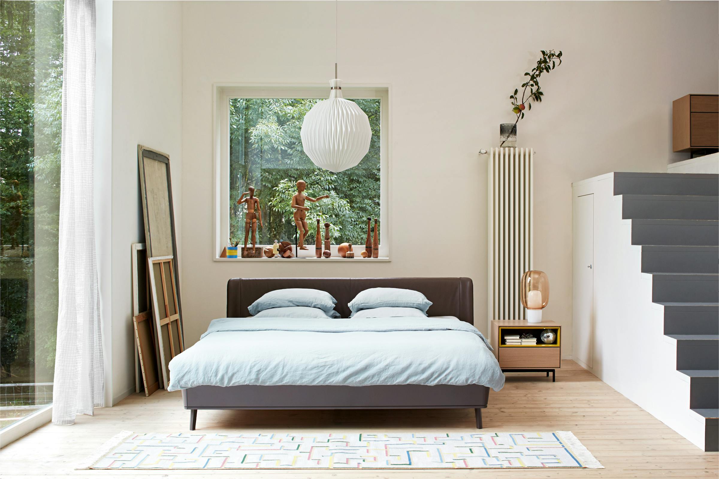 Large bed with backrest in a high-ceilinged room with white pendant lamp