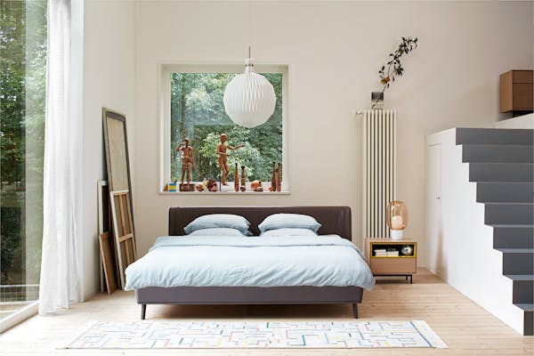 Large bed with backrest in a high-ceilinged room with white pendant lamp