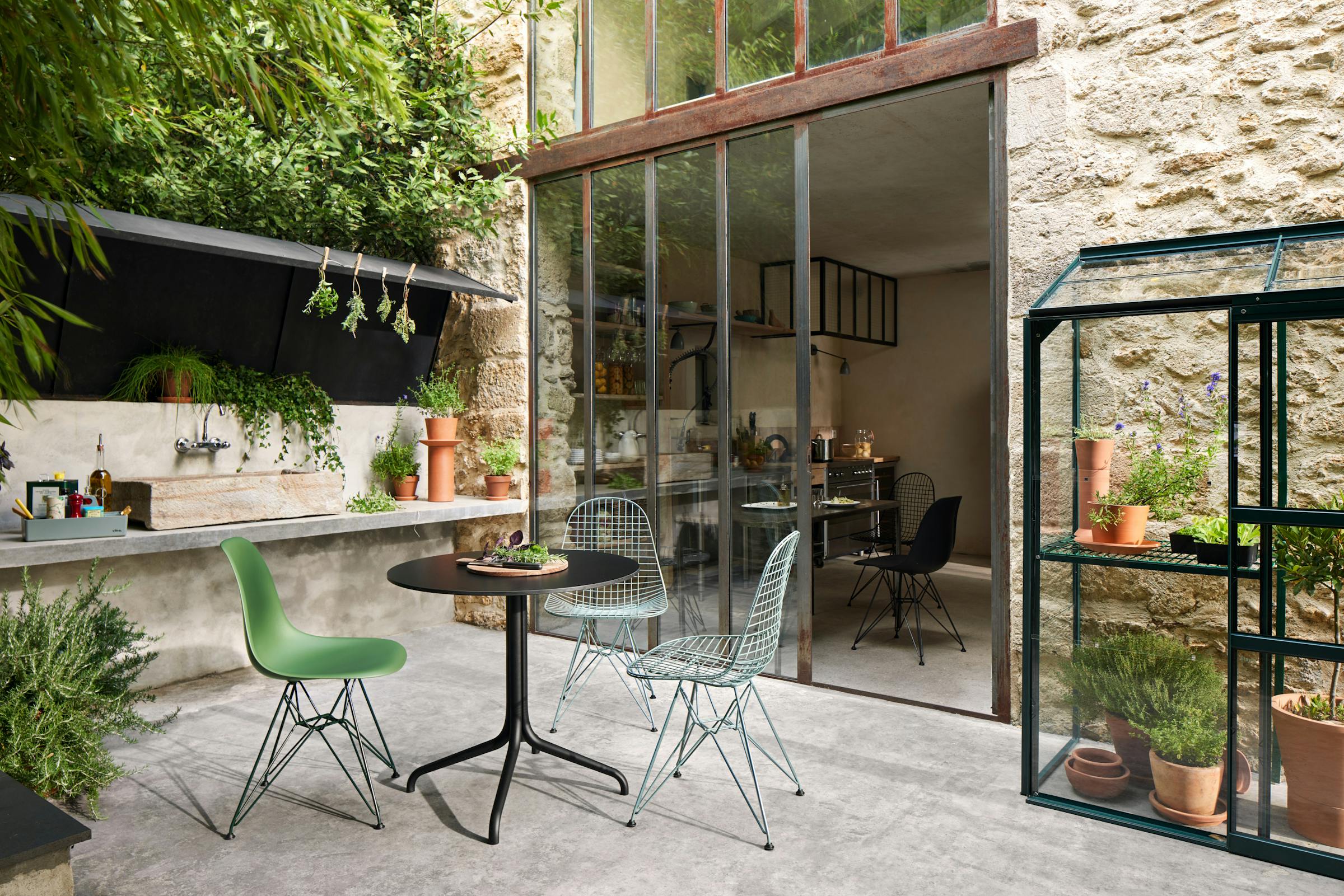 Summer table in the courtyard with three colourful Eames chairs and herbs in the background