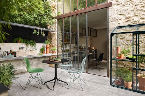 Summer table in the courtyard with three colourful Eames chairs and herbs in the background