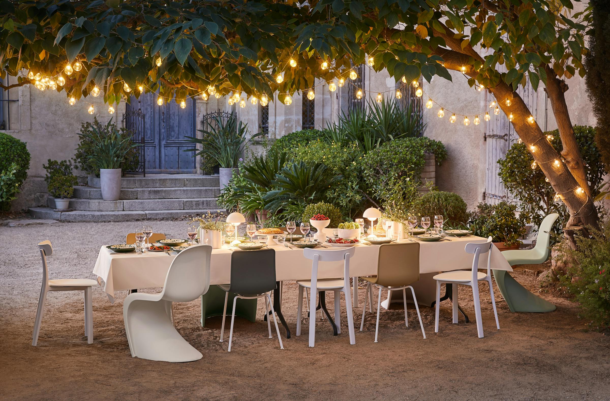 Evening table under a tree with lights and various vitra chairs at dusk