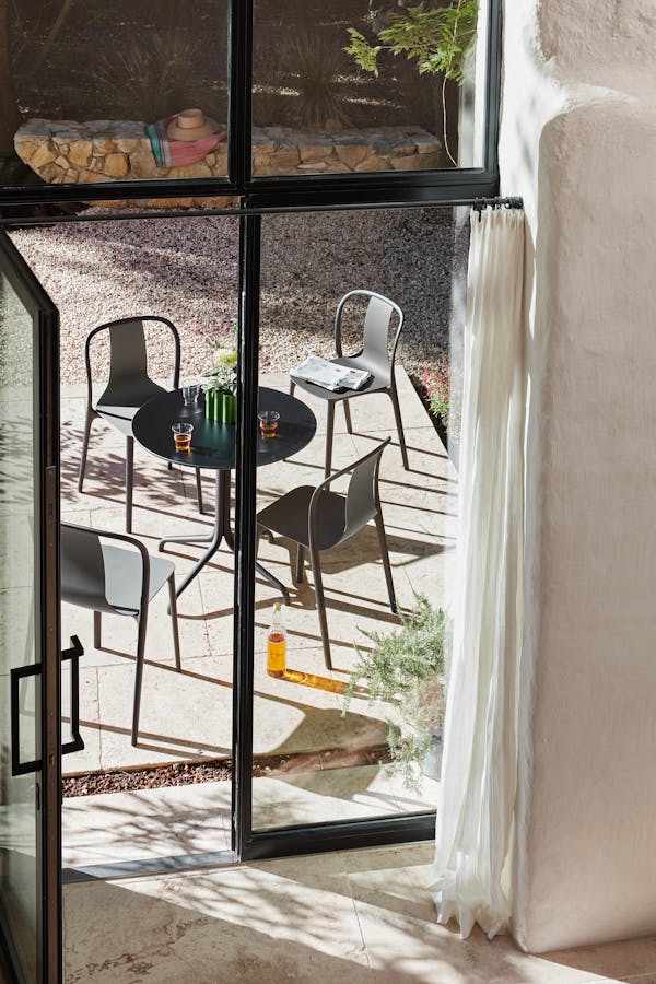 View from inside looking out through a window. Outside stands a round black table with four chairs in bright sunlight.