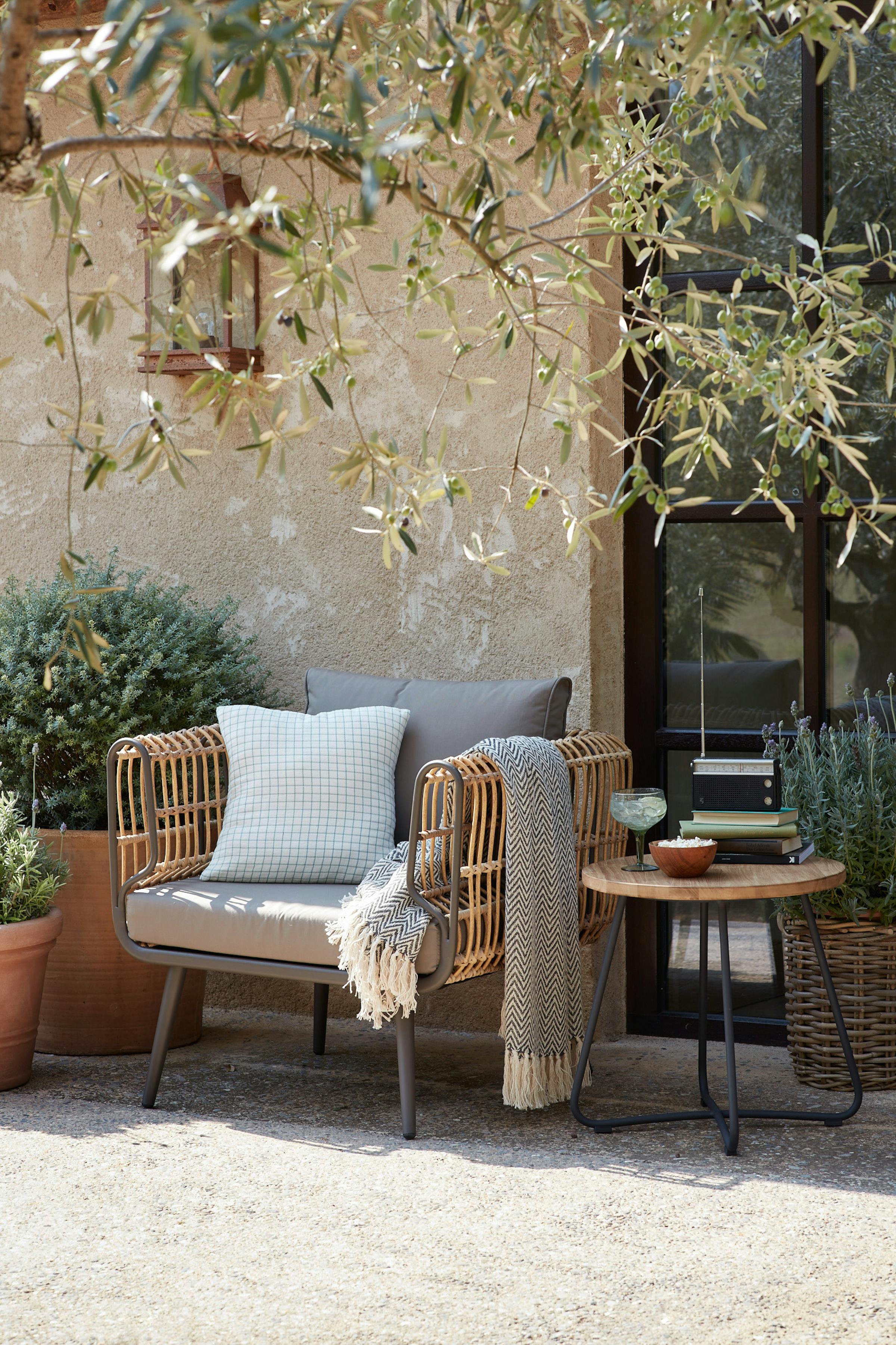 Wicker chair with cushion and a drink on the side on a sunny terrace
