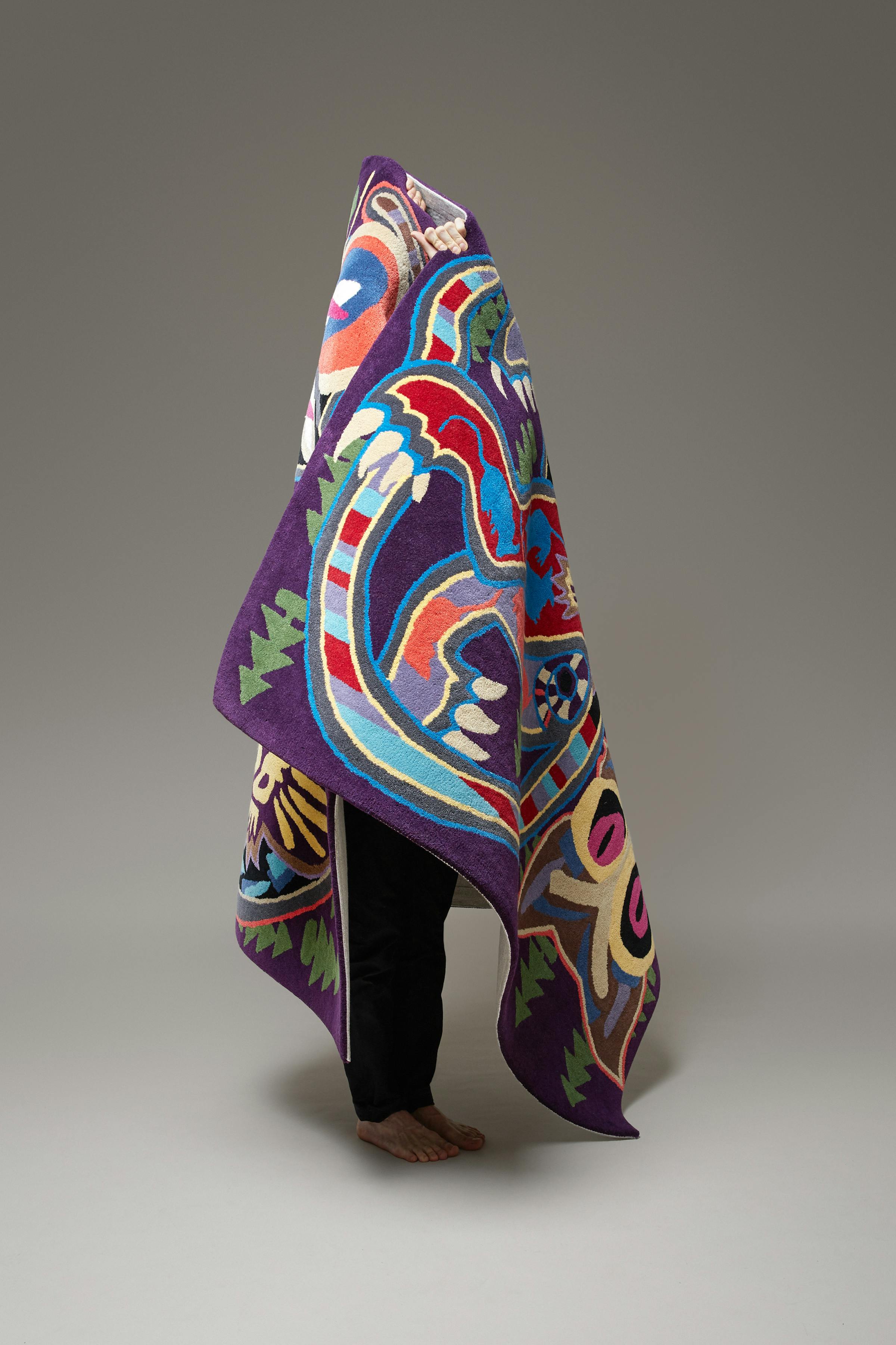 A man in black trousers carries a colourful red and purple cone-shaped carpet.