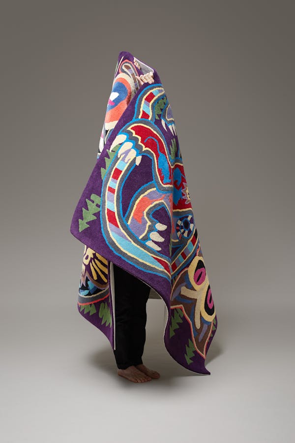 A man in black trousers carries a colourful red and purple cone-shaped carpet.