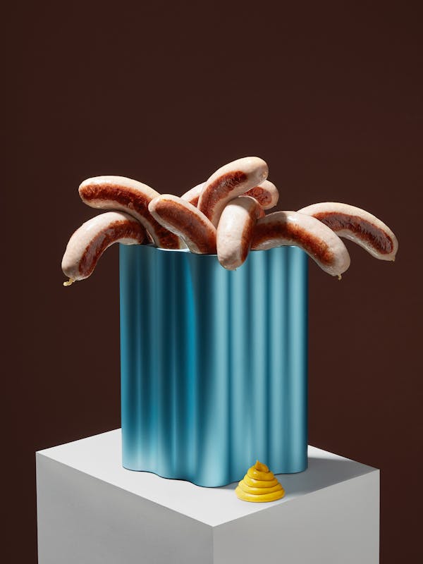 A bright blue nuage vase by the Bouroullec brothers, filled with sausages and a golden yellow ring of mustard on the side.