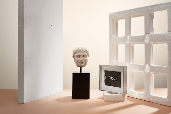 Ancient greek head and the text lines "I Doll" in a set design made out of white styrofoam objects
