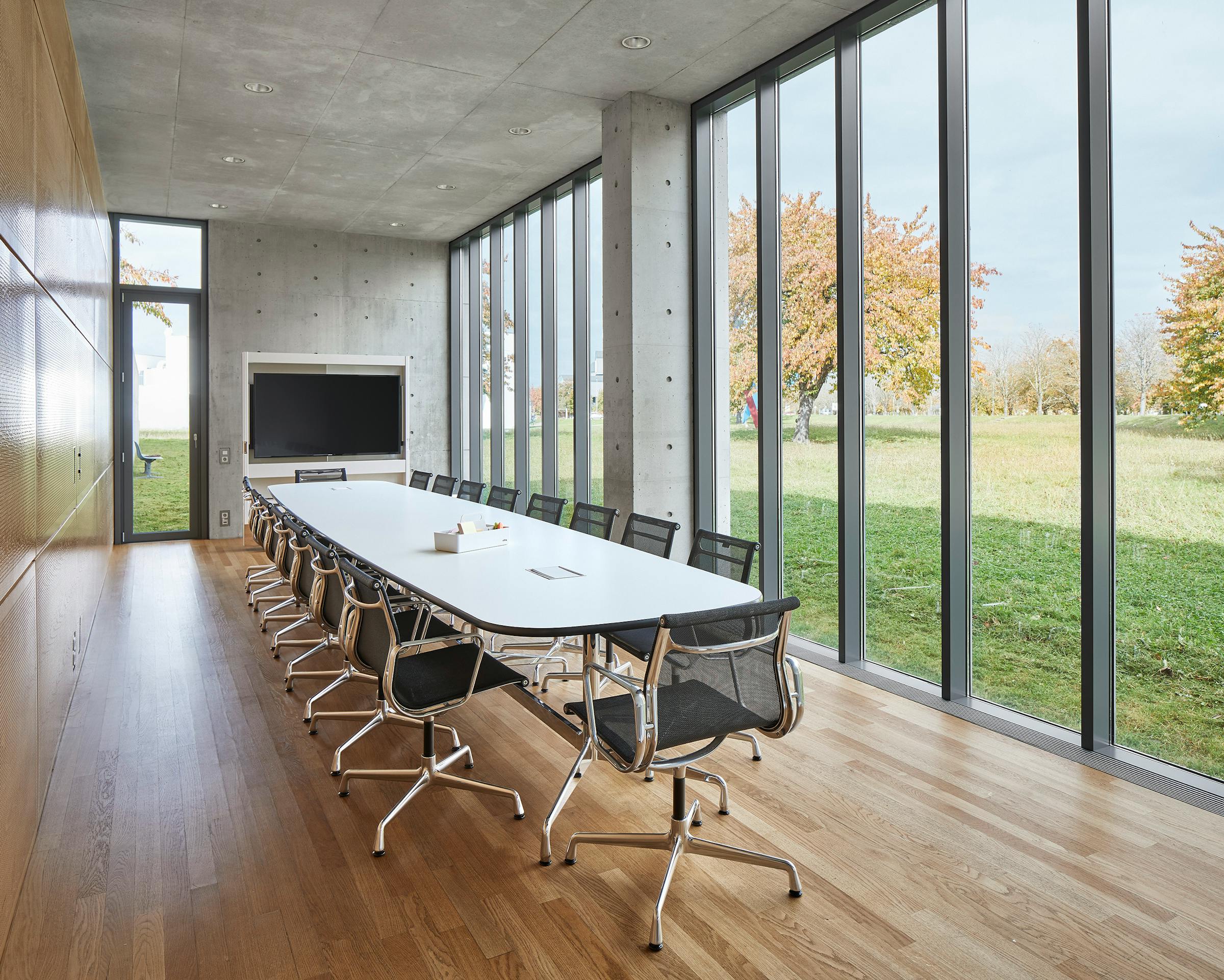 Meeting room of the Tadao Ando Pavilion at the vitra campus in Weil am Rhein with long white table surrounded by Eames chairs and view of the garden