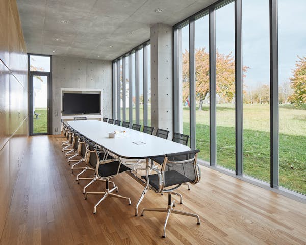 Meeting room of the Tadao Ando Pavilion at the vitra campus in Weil am Rhein with long white table surrounded by Eames chairs and view of the garden