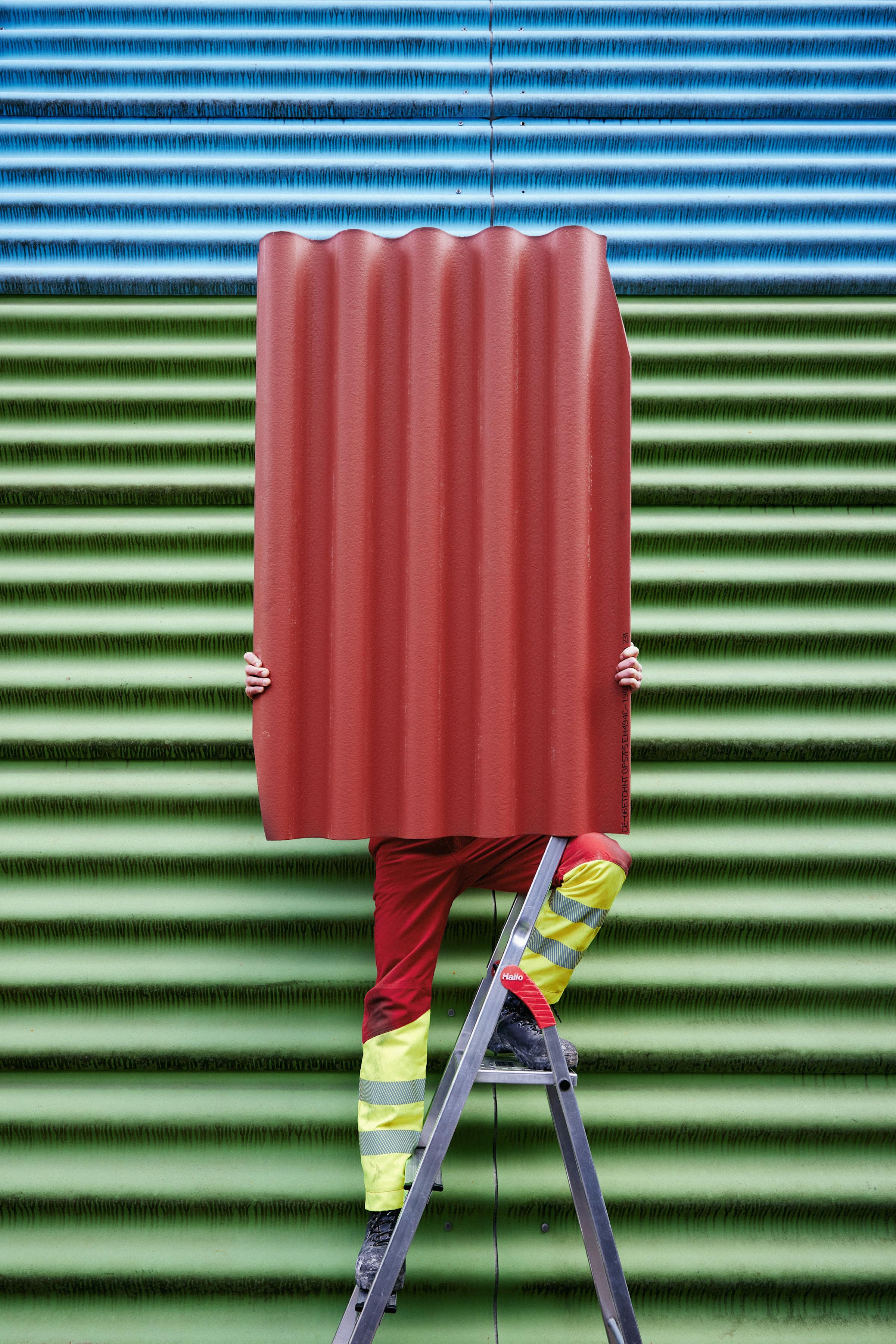 Worker in front of a blue and green  eternit wall holding a red eternit panel