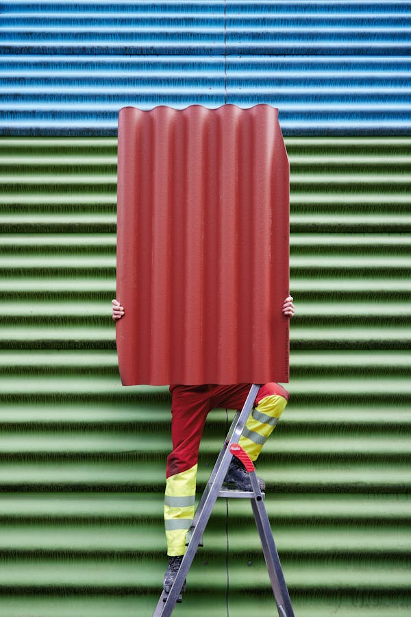 Worker in front of a blue and green  eternit wall holding a red eternit panel