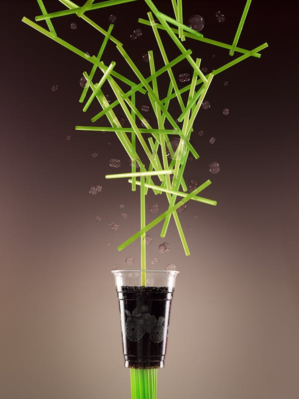 Plastic cup in front of a brown background with many green straws falling from above