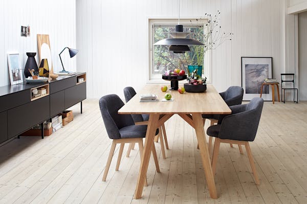 a wooden dining table with a bowl of apples and a long black sideboard