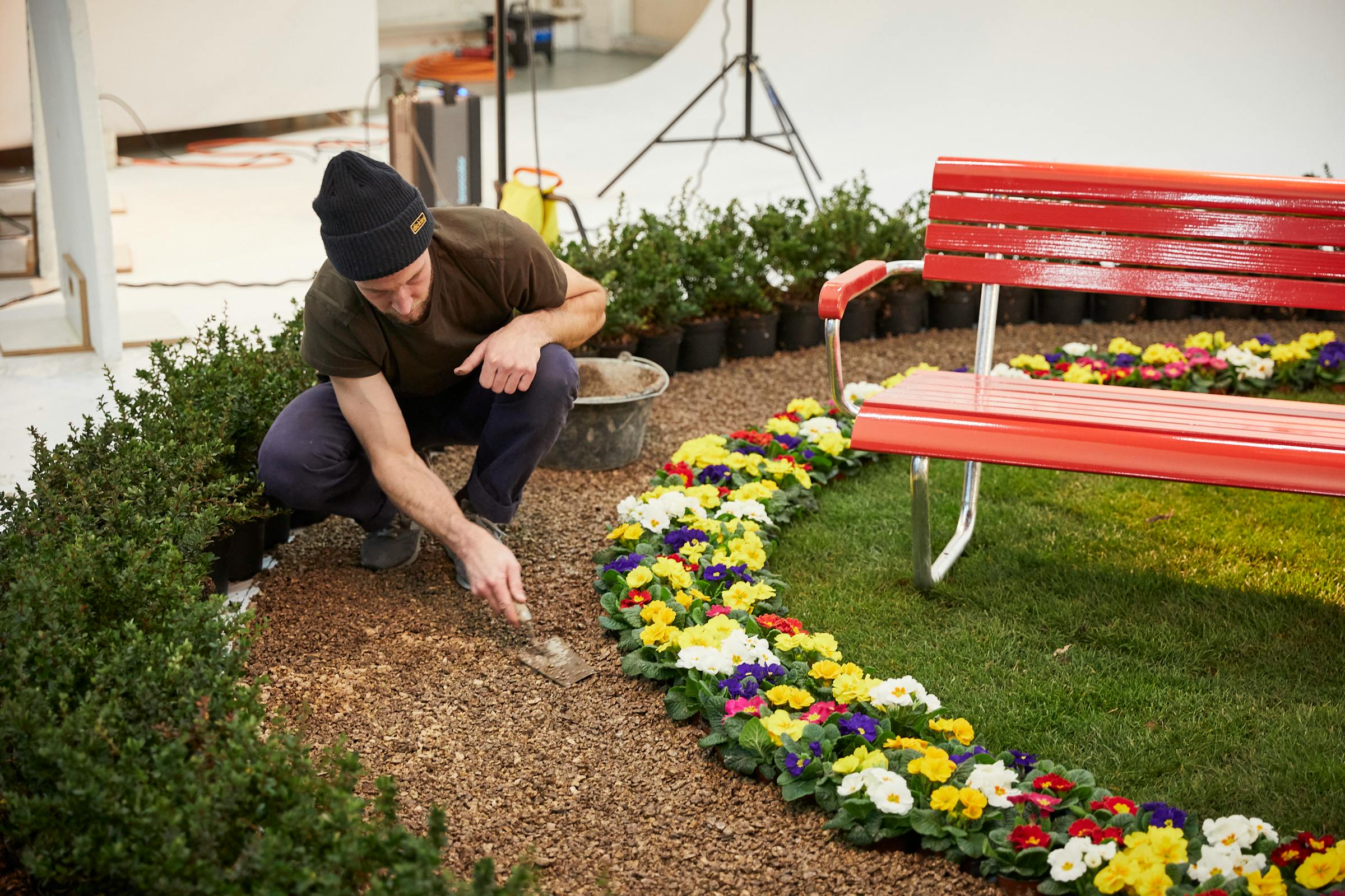 Red bench with a flower bed, a gardener arranges the mulch