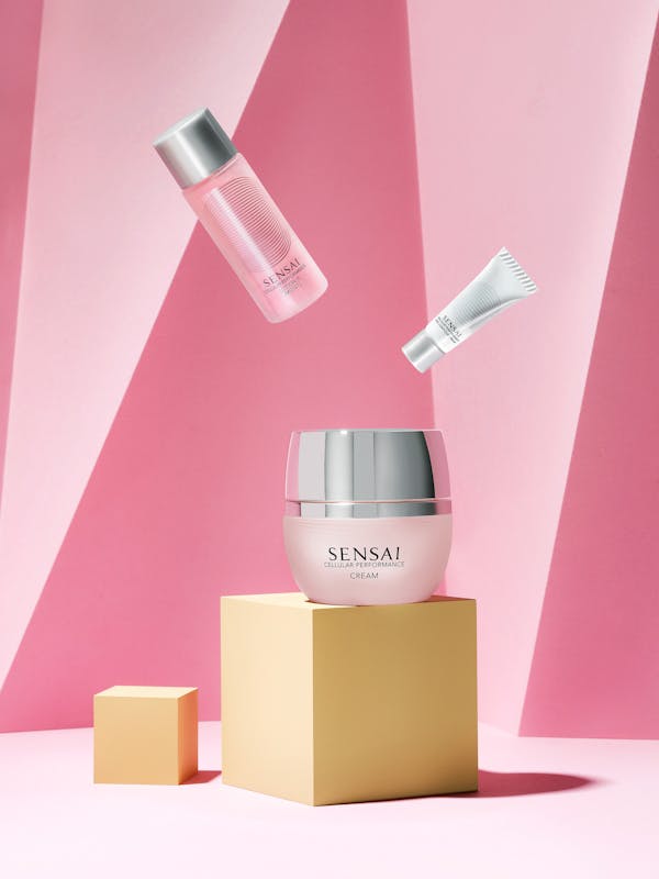 A pink box of beauty cream on yellow cubes in front of a pink paper background