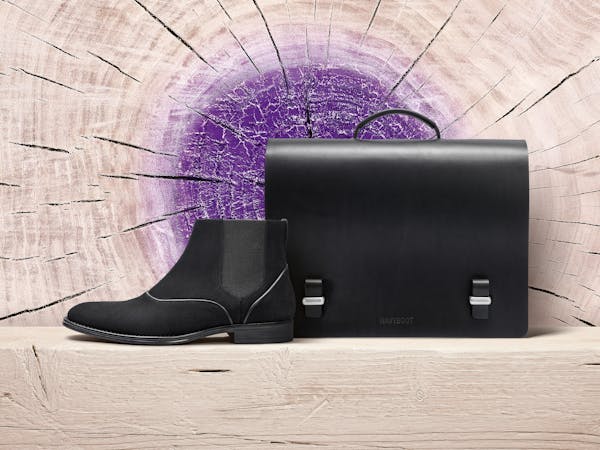 A black men's shoe and a black briefcase in front of a wooden background