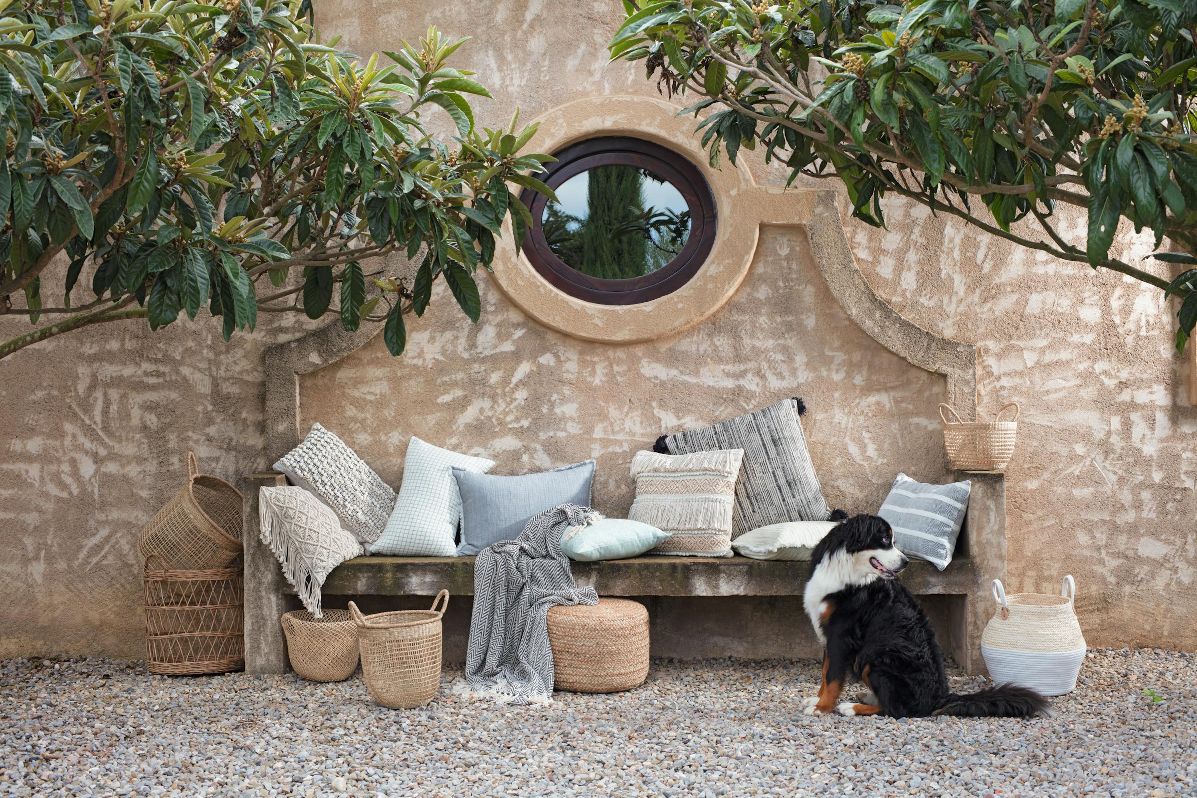 Blankets and cushions for the summer arranged on a stone outdoor bench with a dog

