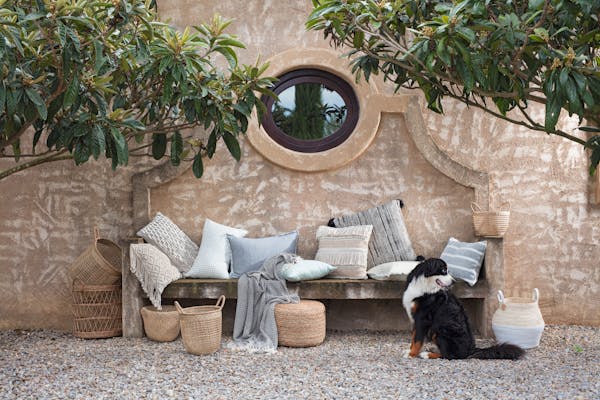 Blankets and cushions for the summer arranged on a stone outdoor bench with a dog

