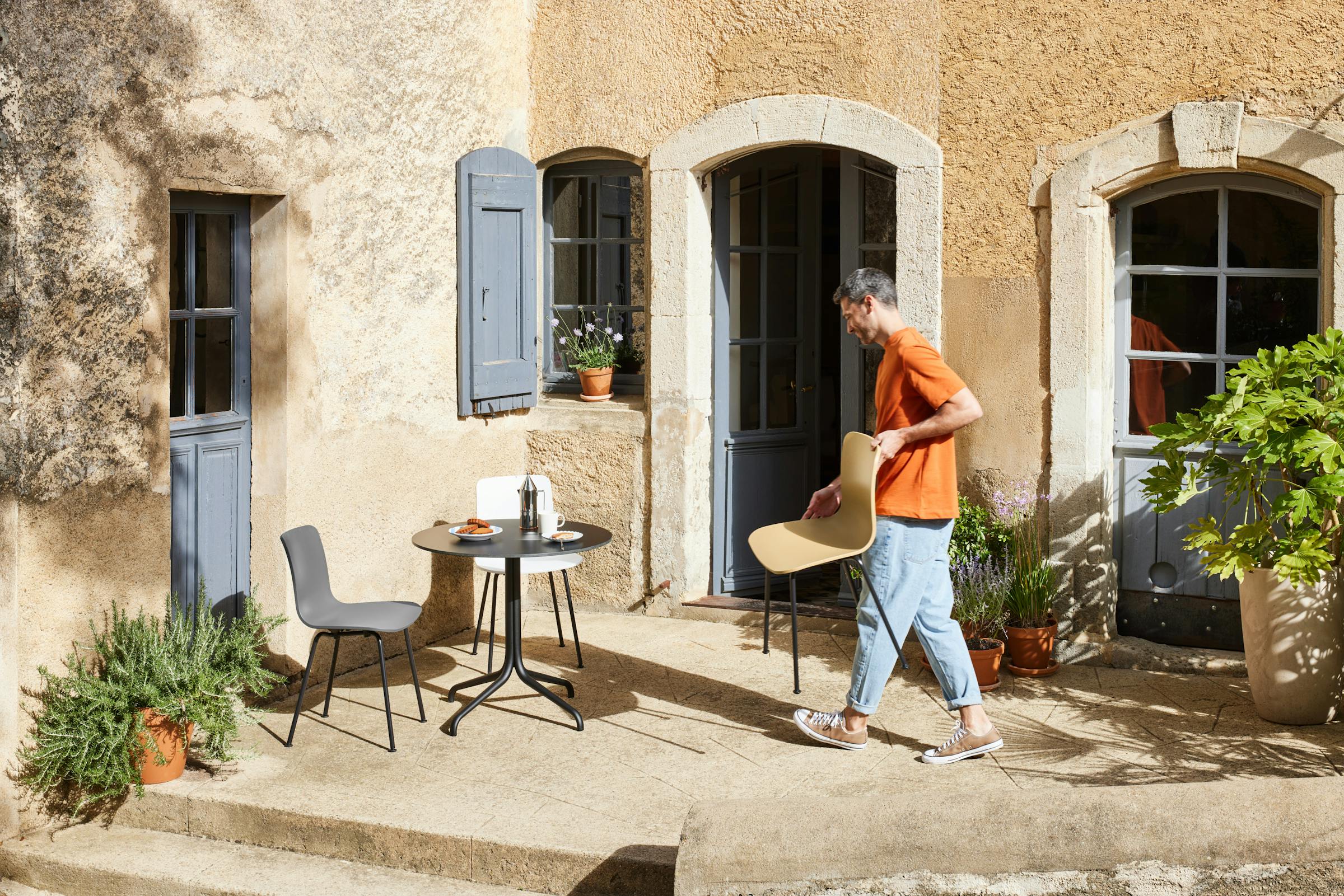 Small table in a courtyard in the south of France, a man carries a chair by Jasper Morrison towards it