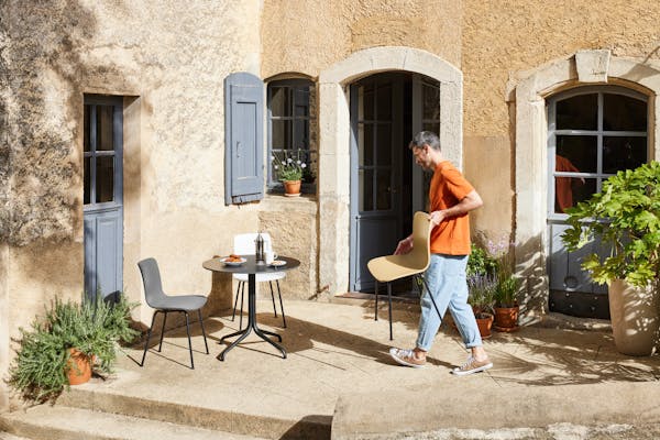 Small table in a courtyard in the south of France, a man carries a chair by Jasper Morrison towards it