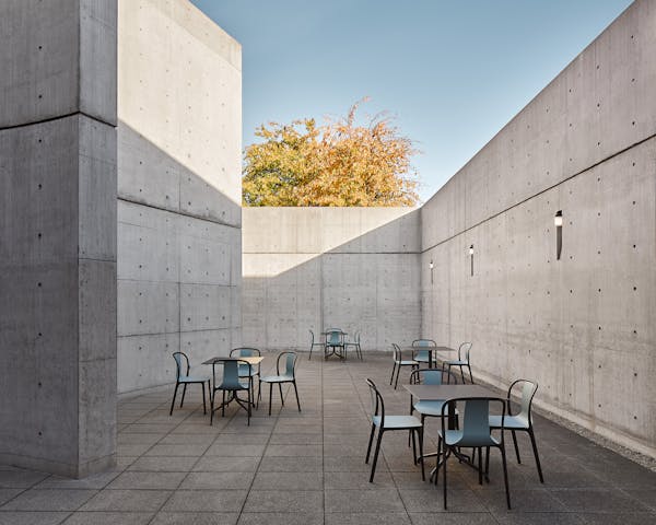 Concrete courtyard of the Tadao Ando Pavilion at the vitra campus in Weil am Rhein in autumn sunshine with four outdoor tables and chairs by the Bouroullec brothers