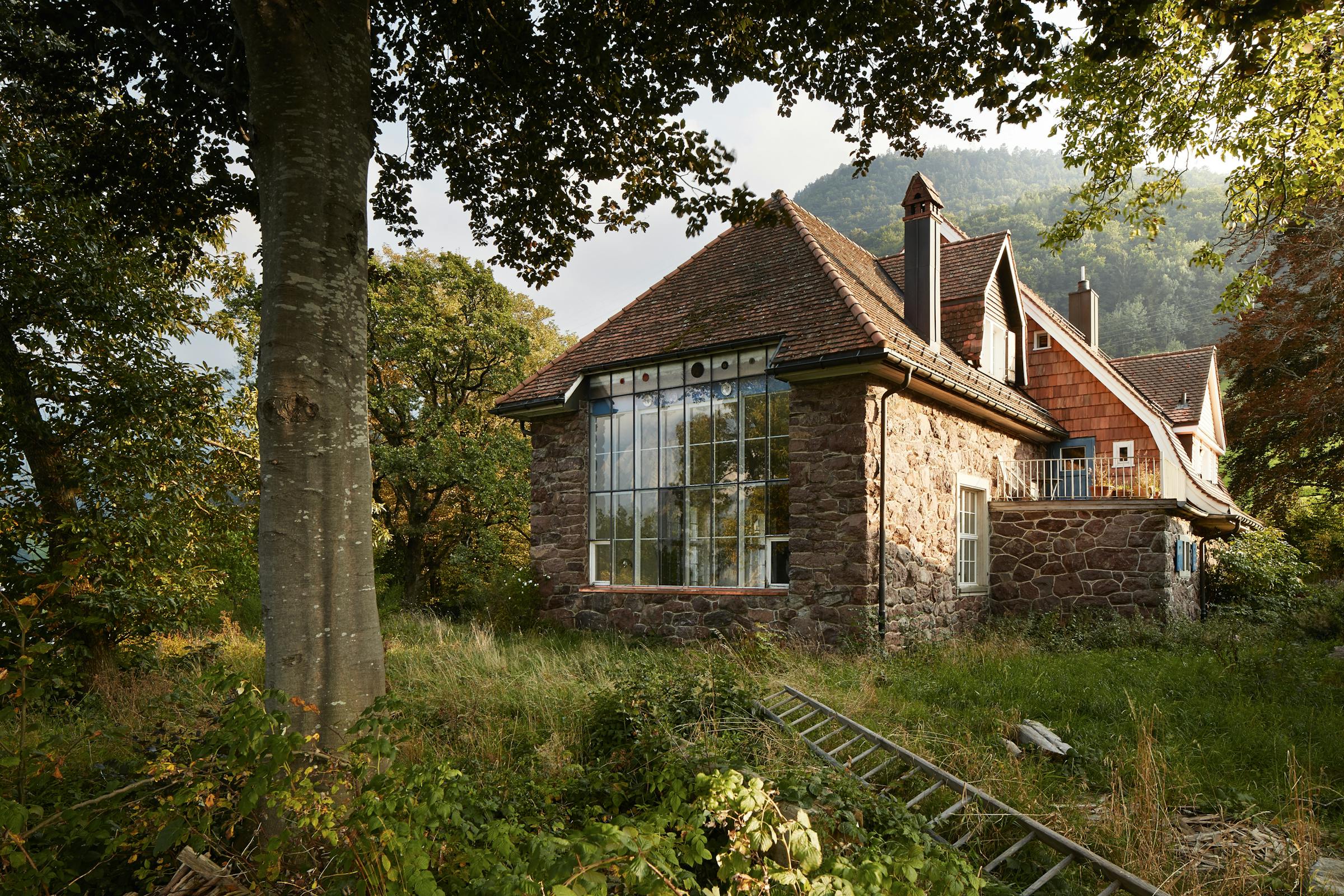 A large stone studio building from the 19th century surrounded by old trees and a meadow.