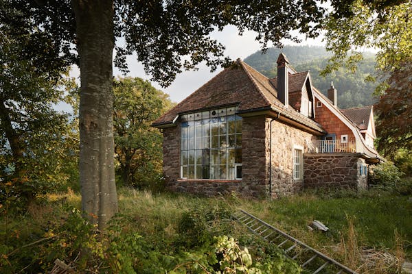 A large stone studio building from the 19th century surrounded by old trees and a meadow.