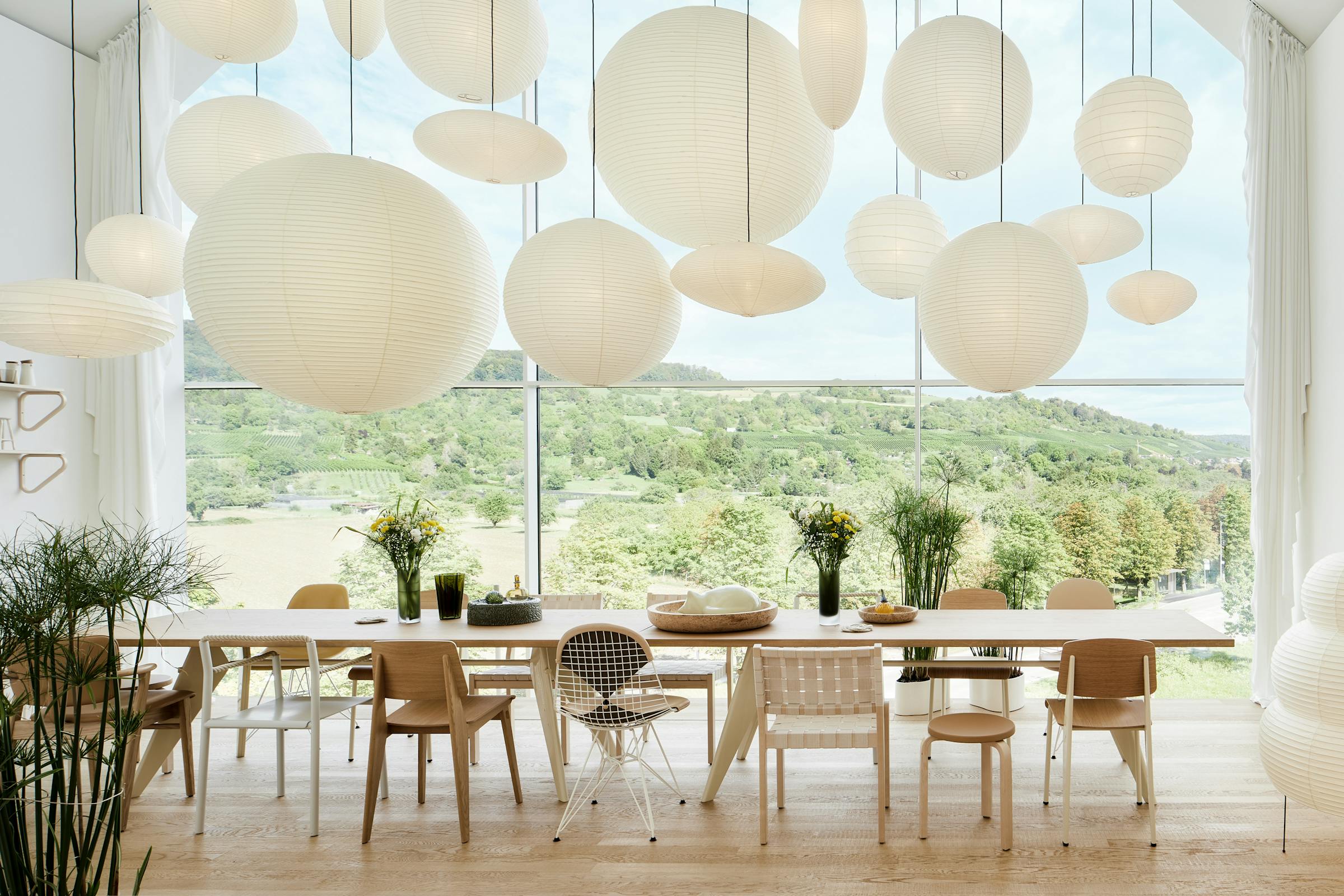 Long dining table with lots of Akari pendant lights and a view of the countryside