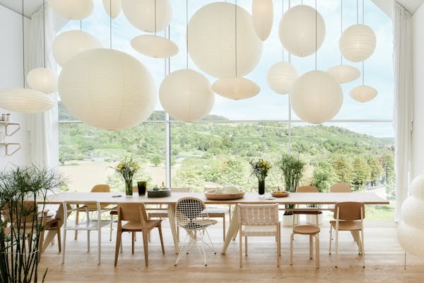 Long dining table with lots of Akari pendant lights and a view of the countryside