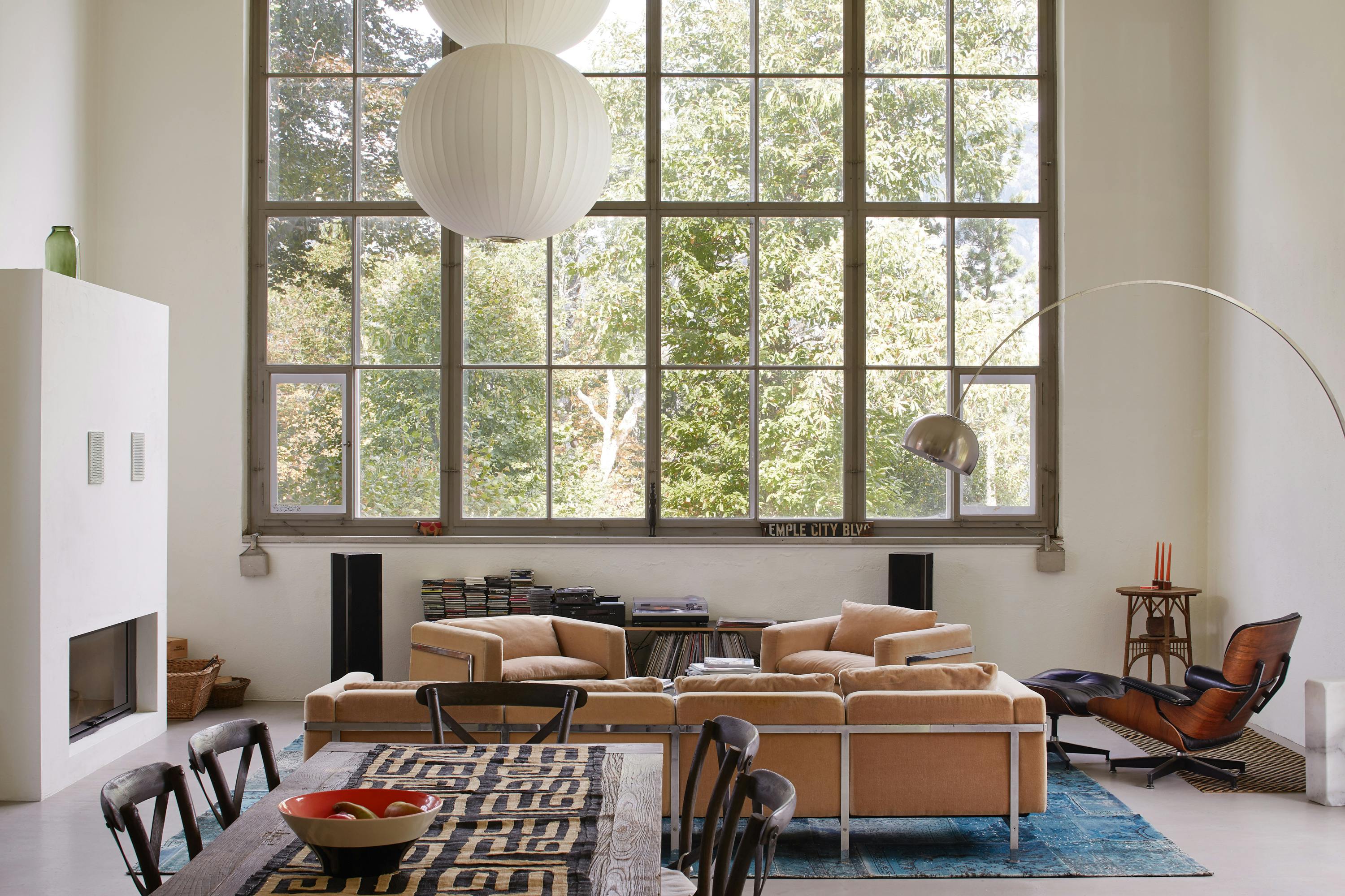 A sofa with several armchairs in front of a huge studio window overlooking greenery