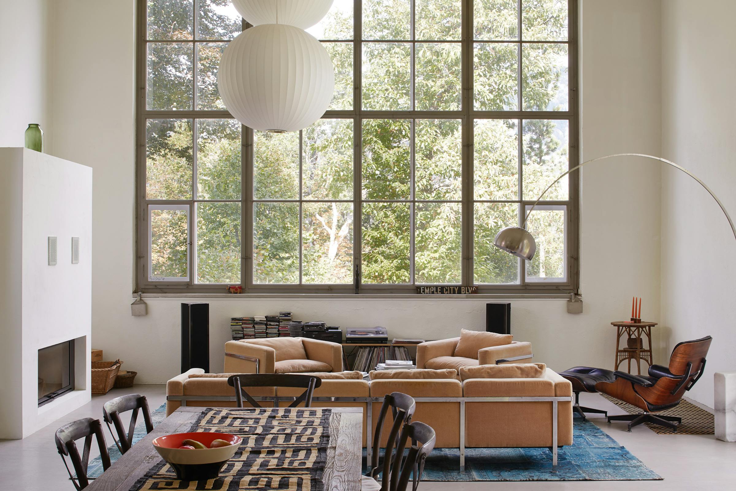 A sofa with several armchairs in front of a huge studio window overlooking greenery