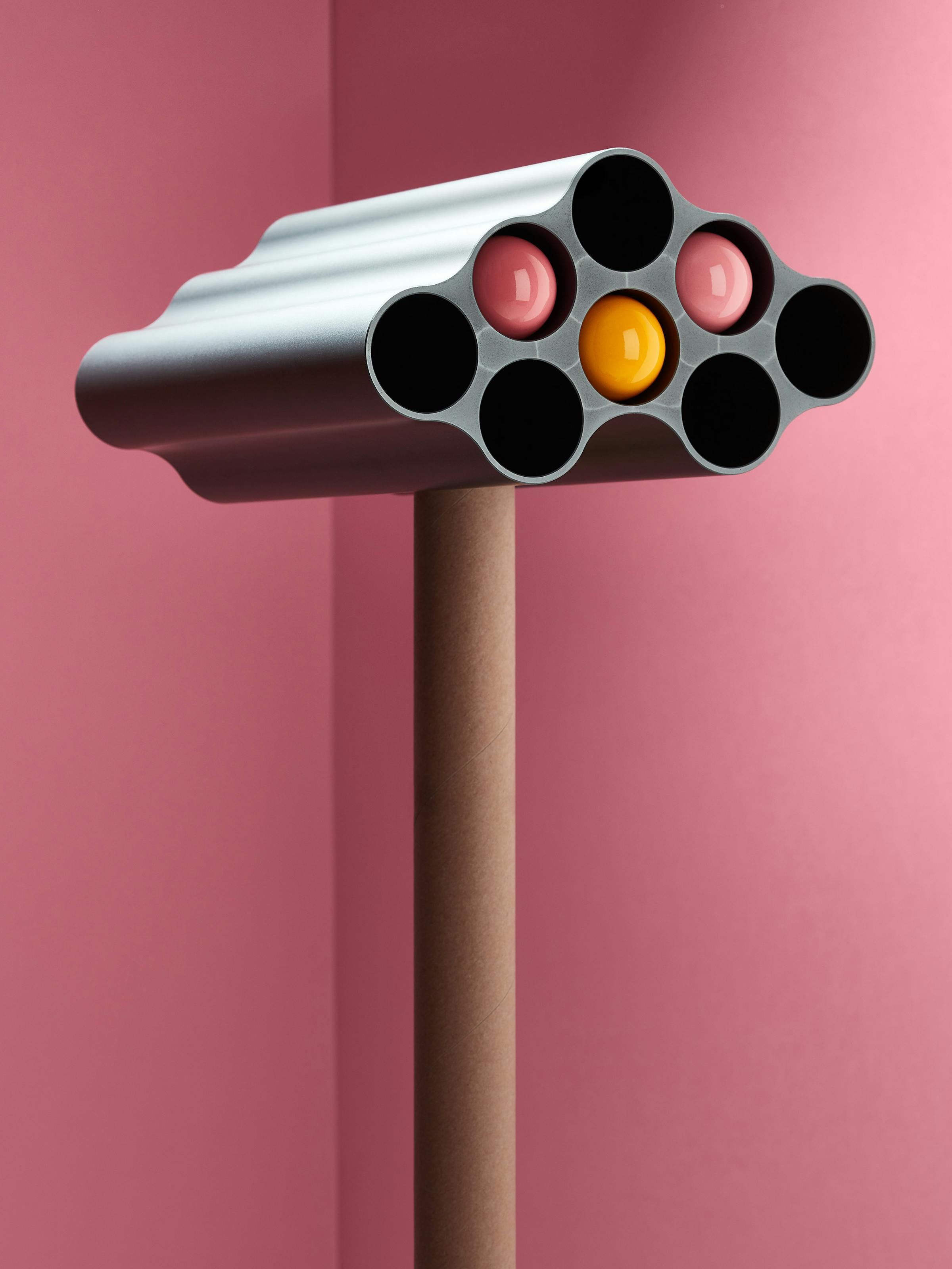 A grey nuage vase by the Bouroullec brothers with colored wall dots in it in front of a pink background 