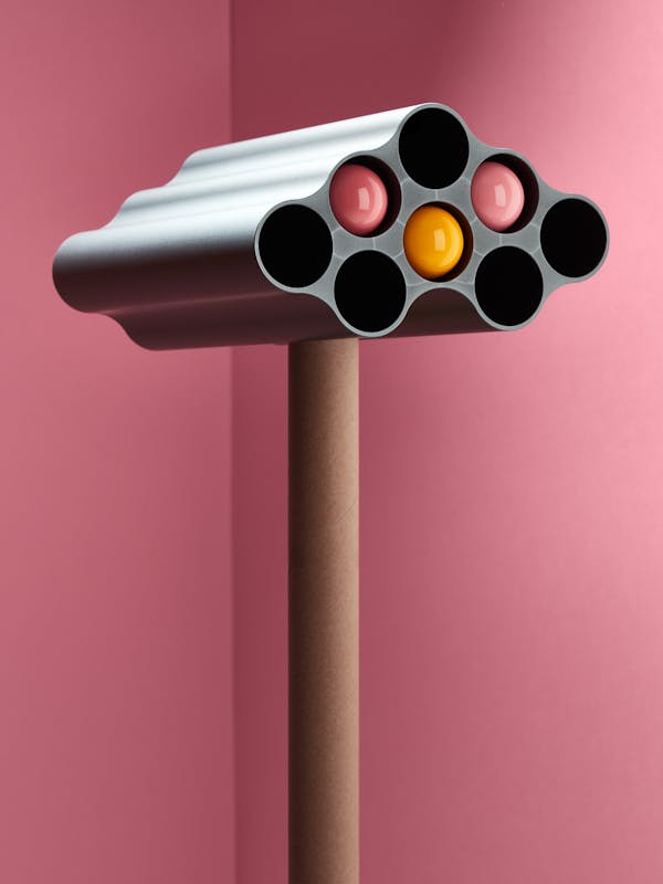 A grey nuage vase by the Bouroullec brothers with colored wall dots in it in front of a pink background 