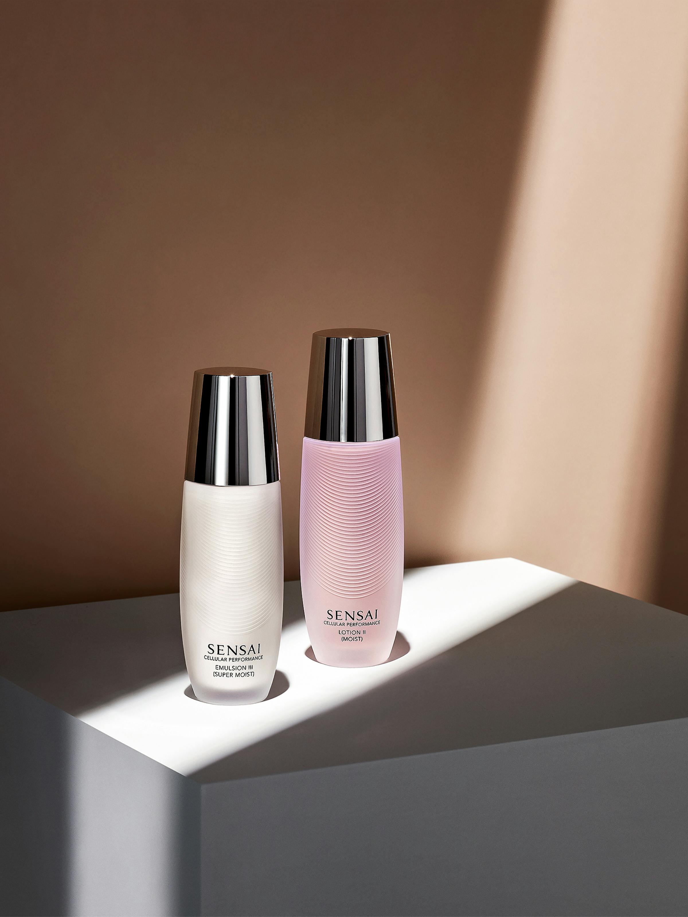 Two glass bottles of beauty creams on a grey pedestal in front of a beige wall with strong light falling on them