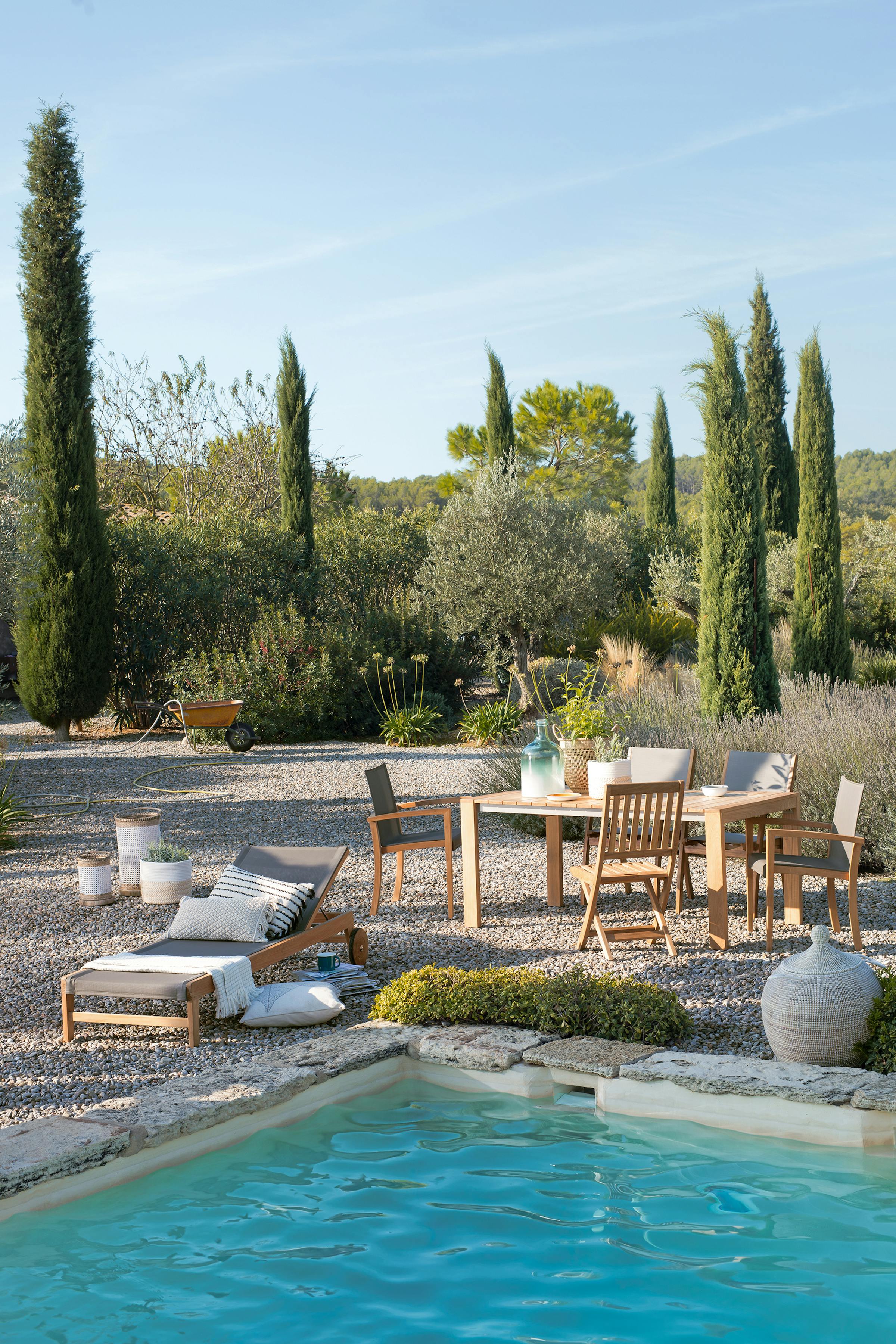 Dining table and sun lounger on gravel with a pool in the foreground