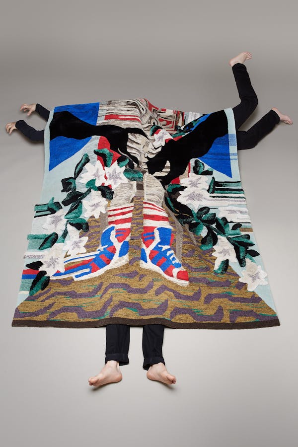 Three men in black trousers crawl under a large carpet with a panther design.