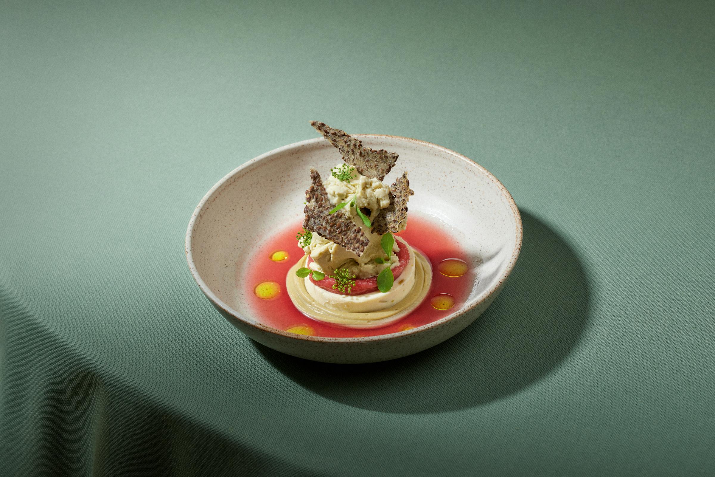 Plate with dessert - a pistacchio ice cream in a rhubarb coulis on a green table cloth