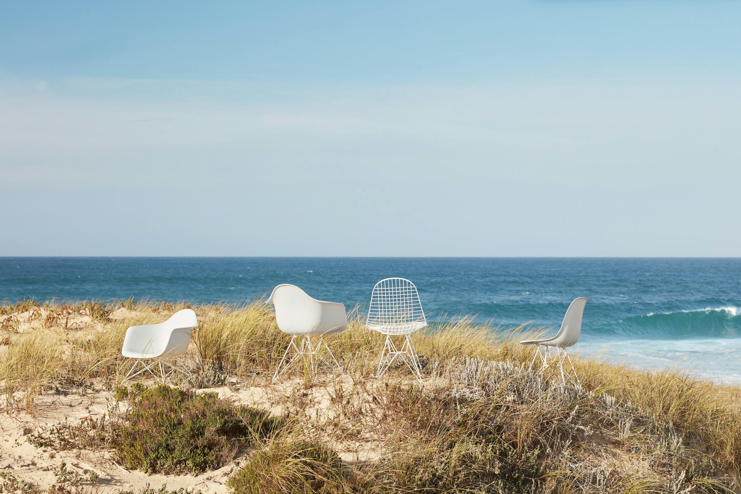 four white Eames chairs in the dunes overlooking the sea