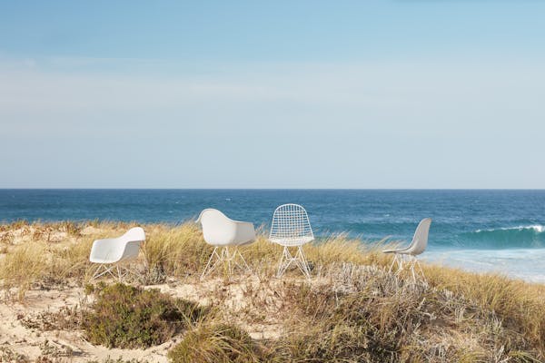 four white Eames chairs in the dunes overlooking the sea