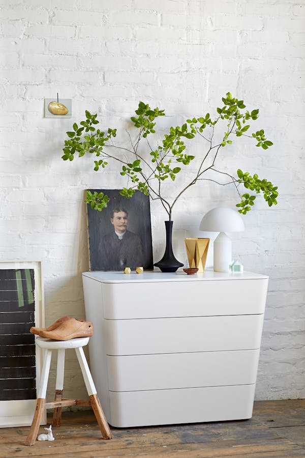 White chest of drawers in front of a white brick wall on a wooden floor