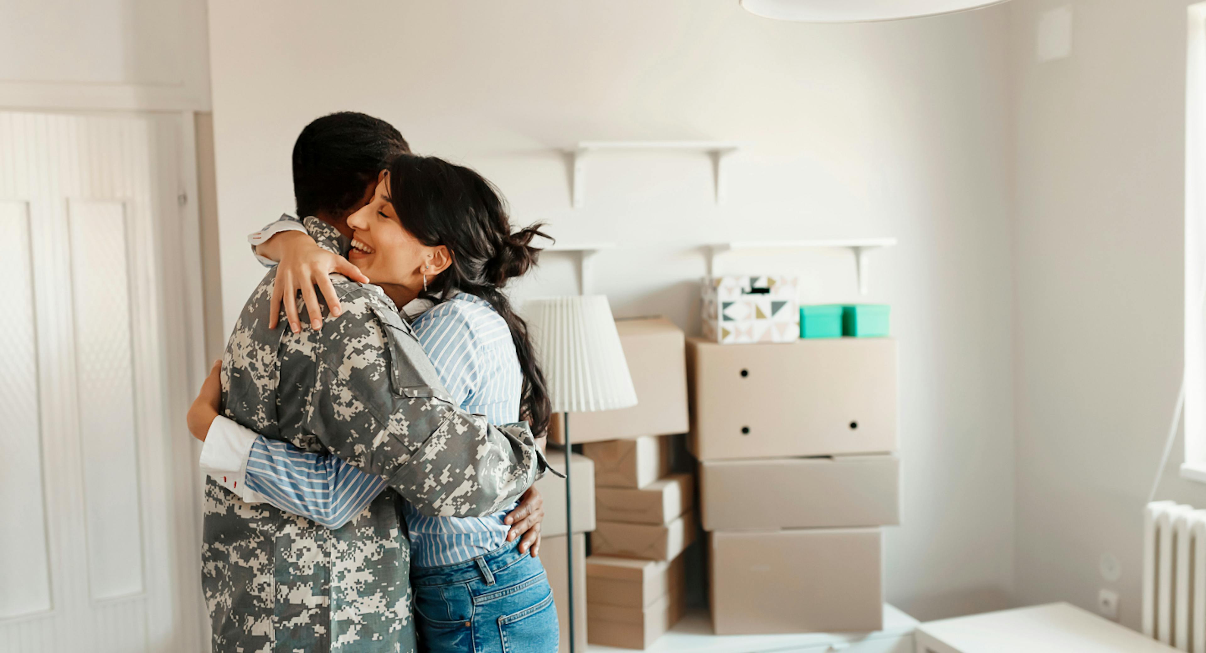 A man wearing a military uniform and woman embracing as they share the joy of moving into a new home.