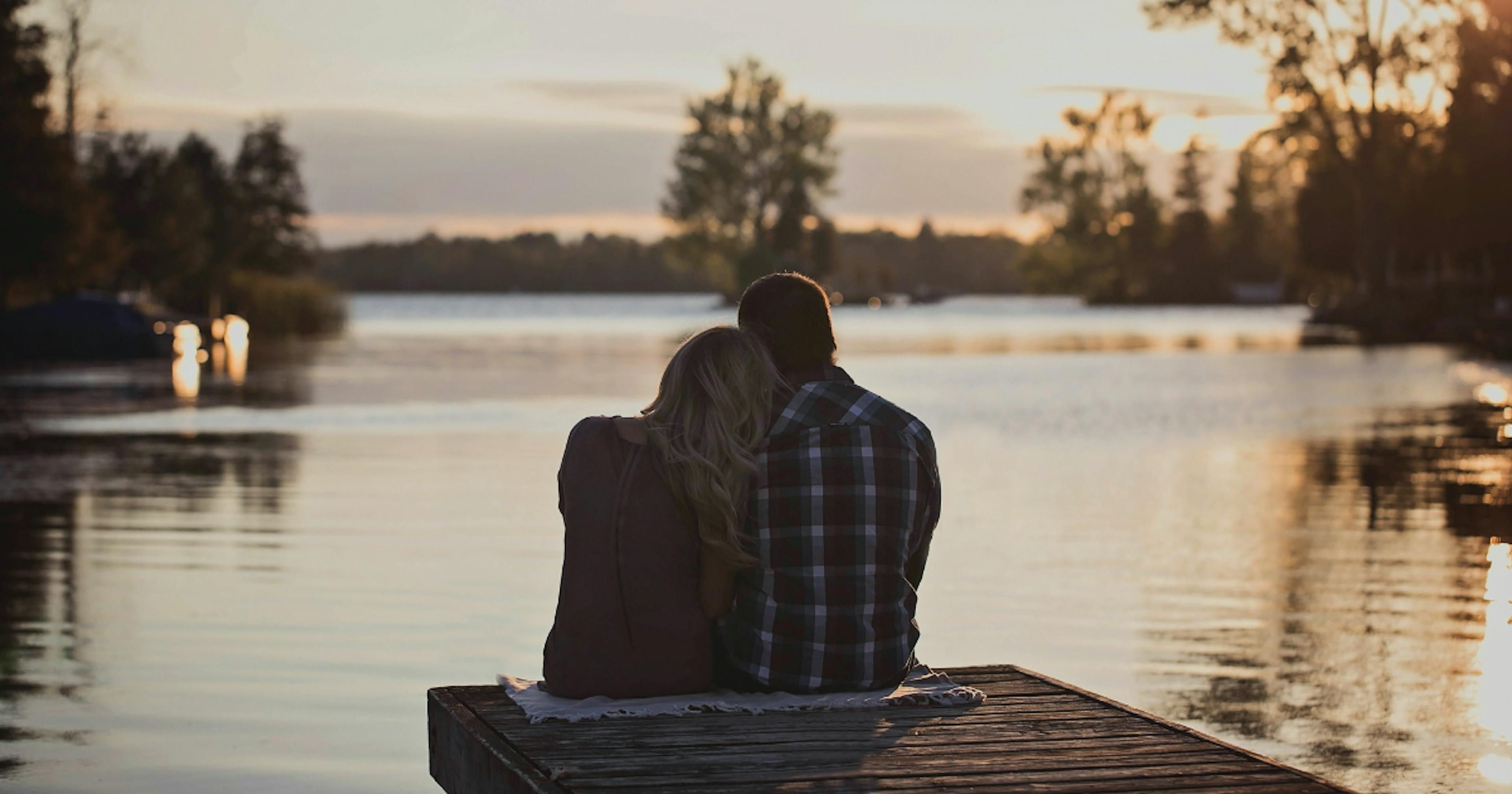 Couple sitting on a dock looking out over a lake.