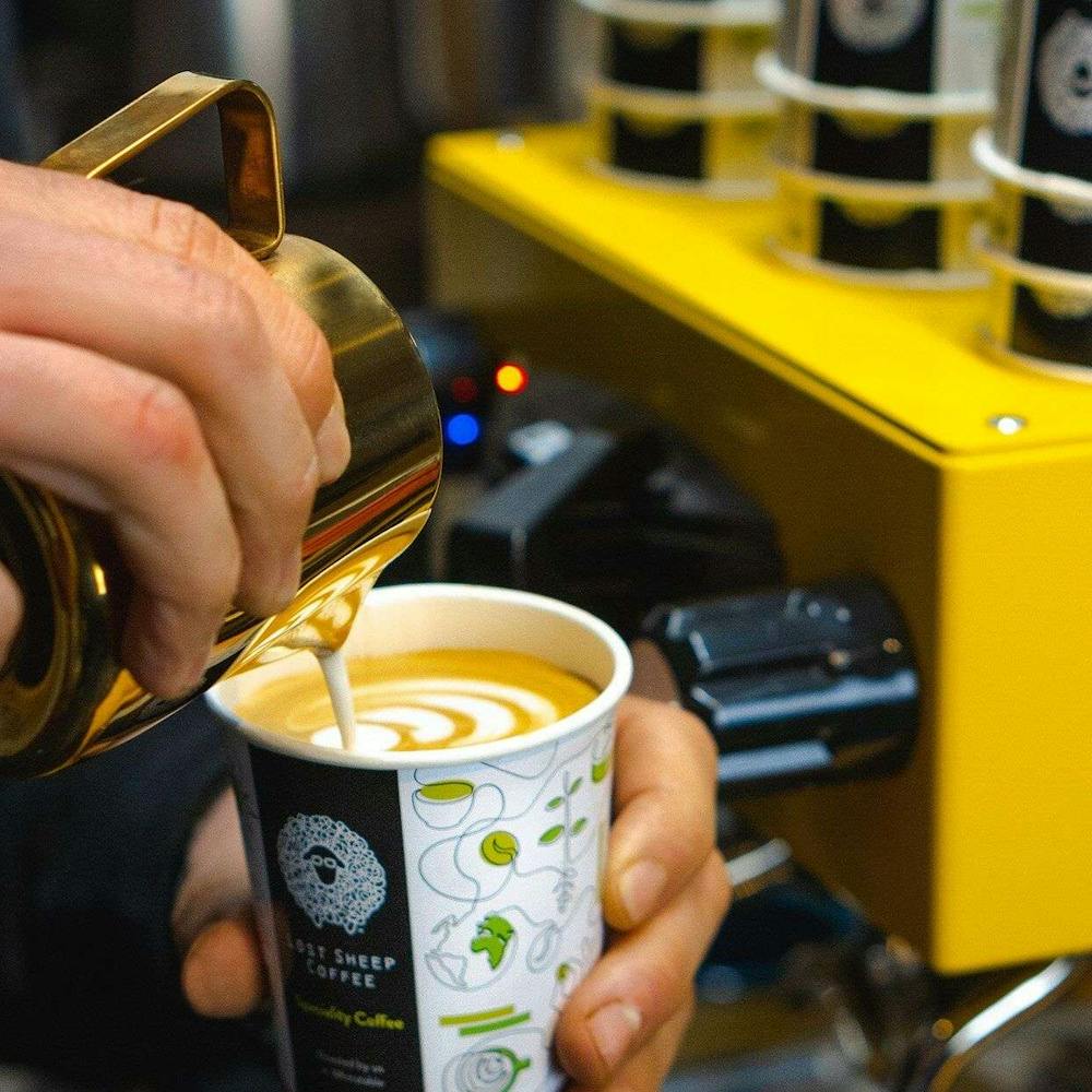 Milk being poured into Coffee cup next to yellow espresso machine