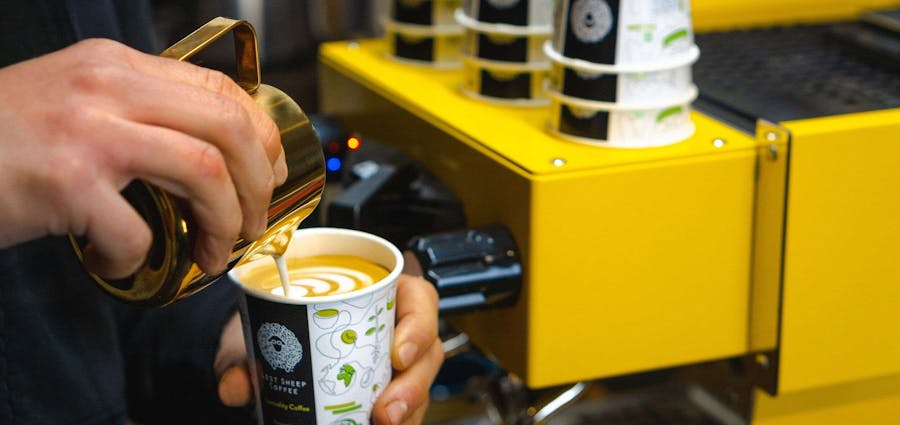 Milk being poured into Coffee cup next to yellow espresso machine