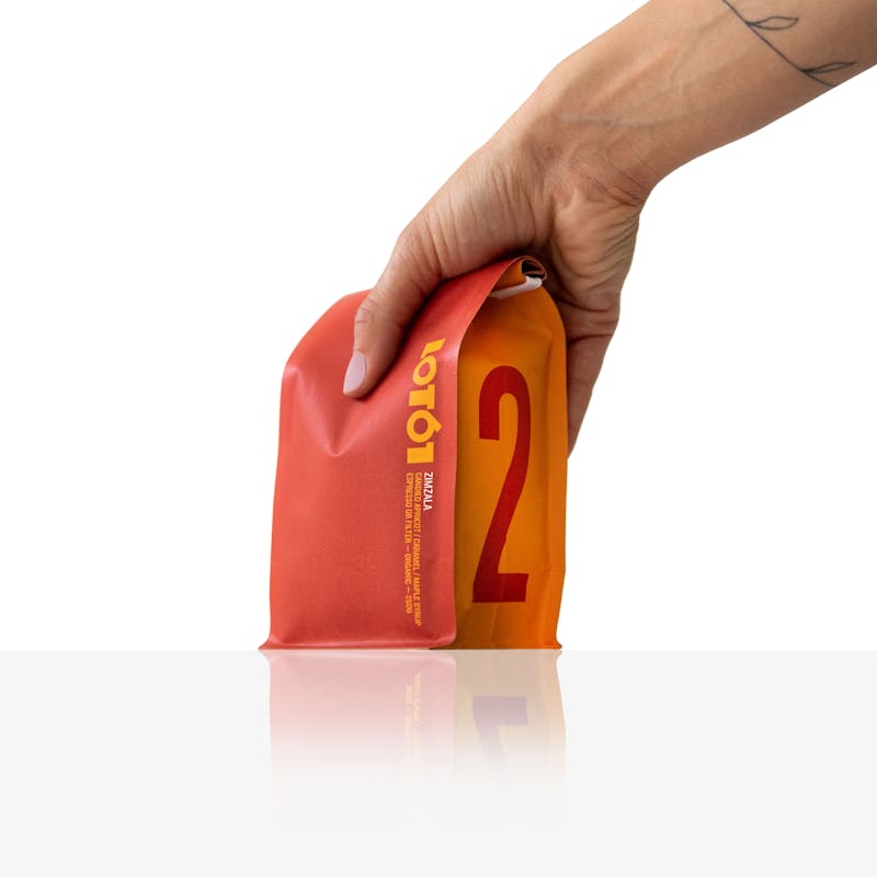 Hand holding down on orange colored LOT61 coffee packaged for Zimzala product