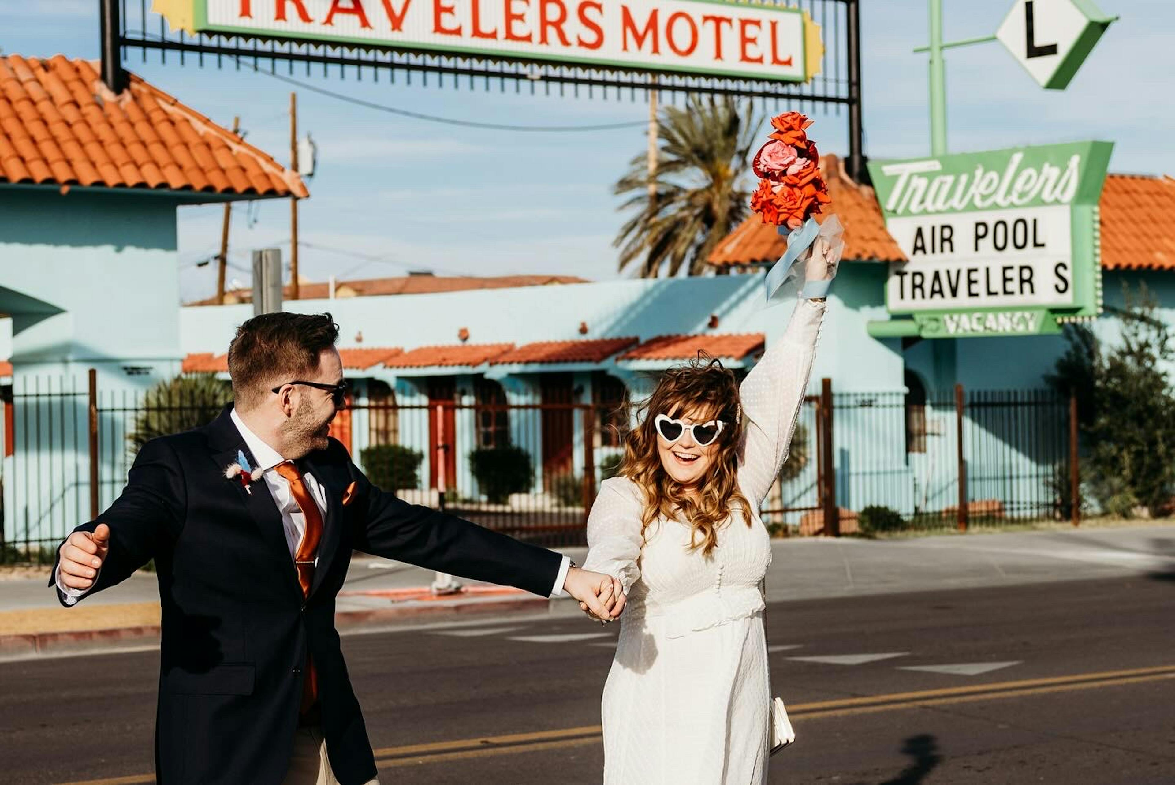 photo from real bride Hannahs wedding in vegas. She is wearing white heart sunglasses, a white polkadot wedding dress and it holding her bouquet up in celebration and her new husbands hand.