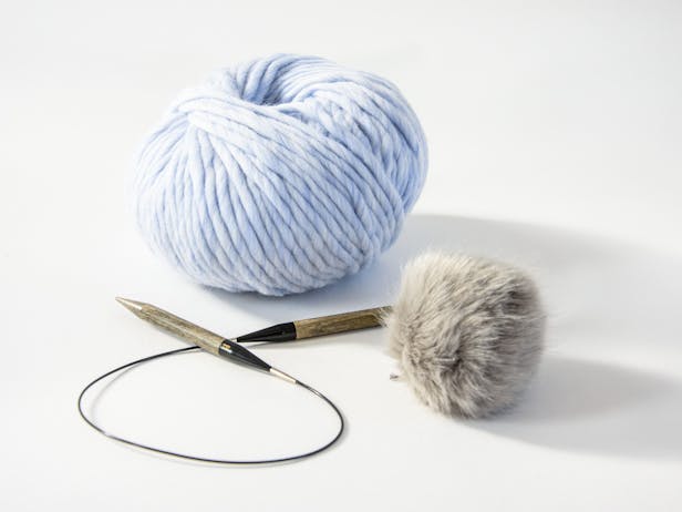 circular knitting needles with super chunky yarn and a faux fur pom pom