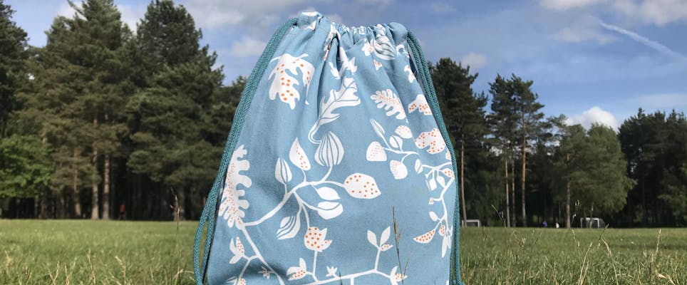Drawstring bag in blue floral cotton in an open field with blue skies