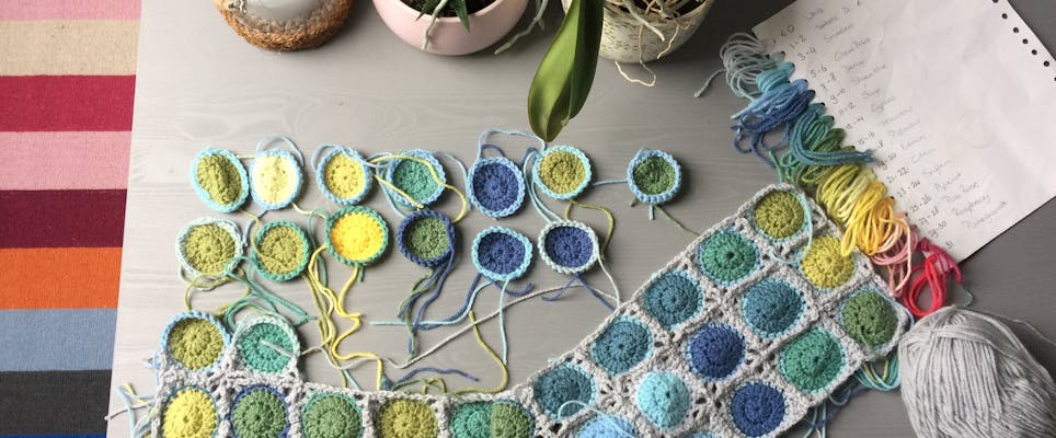 Multicoloured crochet square blanket in progress with labelled colour notes